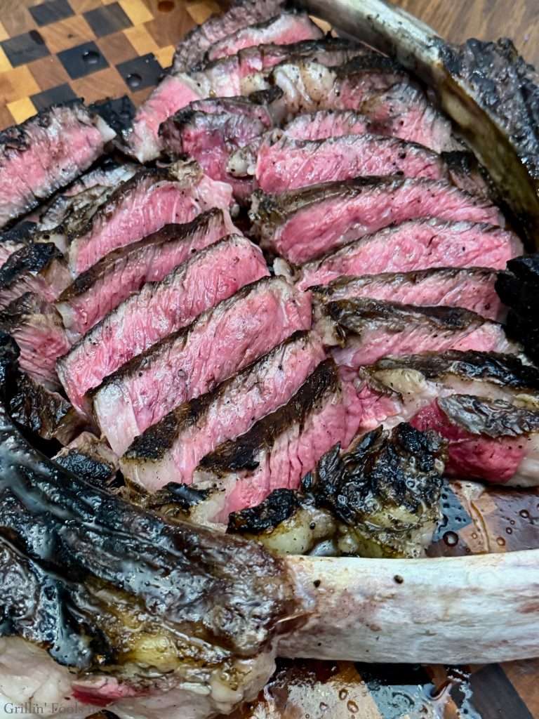 Sliced medium-rare beef roast with pink center and dark crust on a wooden cutting board cooked with the reverse sear method from the Tomahawk Steak Recipe