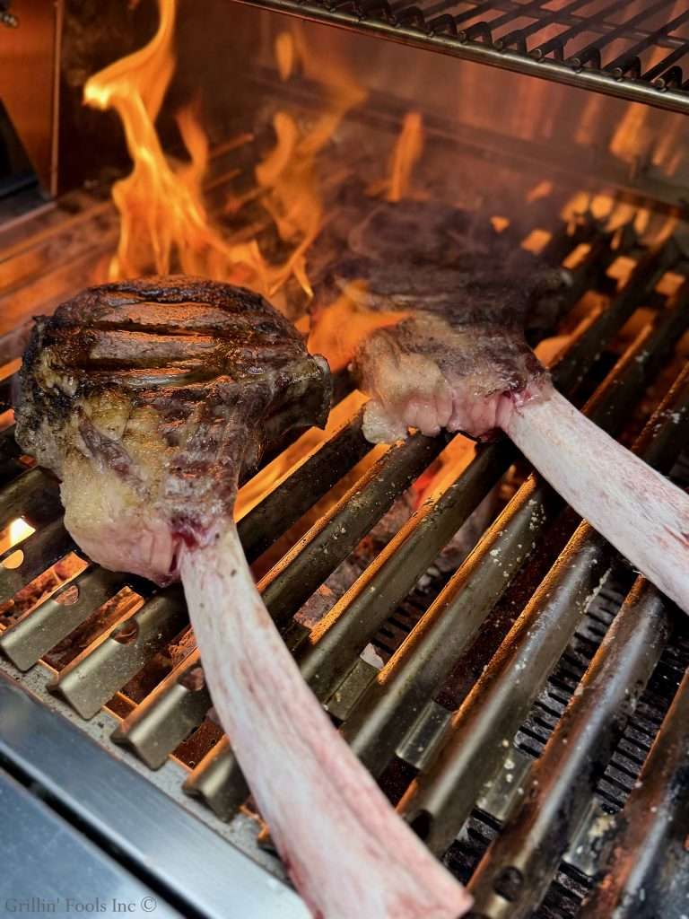 Beef rib bones sizzling on a hot grill over open flames for the sear part of reverse sear for this Tomahawk Steak Recipe