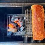 Seasoned pork loin on the upper rack of a grill to the right of a charcoal fire.