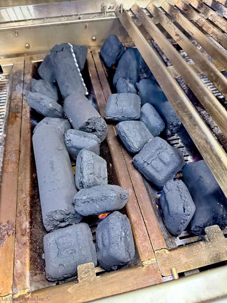 Pile of charcoal briquettes in a barbecue grill, with metal grate bars and a small flame starting to glow.
