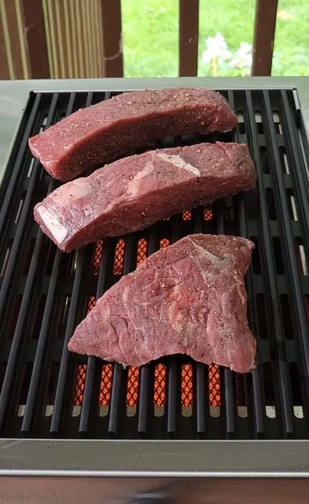 Three raw beef sirloin cap steaks seasoned with salt, pepper and garlic on a and infrared burner.