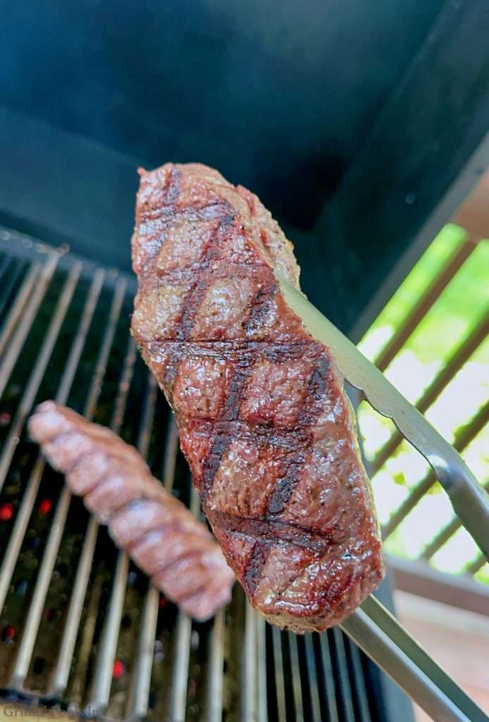 Grilled coulotte steak held over a barbecue grill, close-up shot highlighting char marks and juicy texture