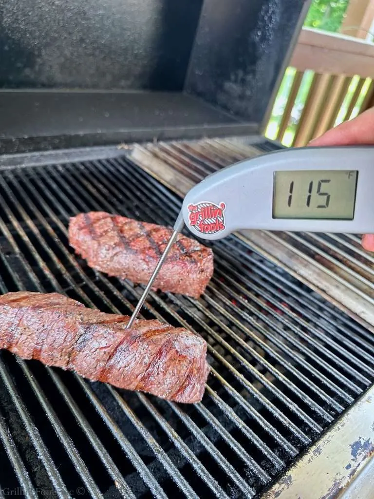 A sirloin cap steak on a grill with charred grill grates and a digital thermometer showing 115°F nearby.