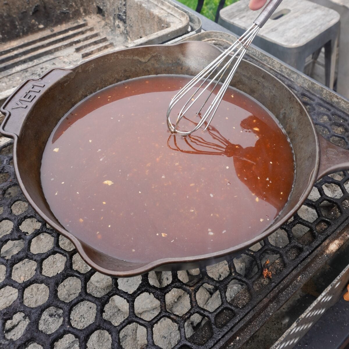 Bourbon sauce in a cast iron skillet over a charcoal grill.