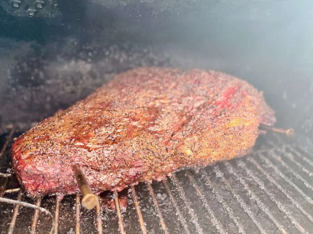 Close-up of a beef brisket with a dark, peppery crust inside a smoker
