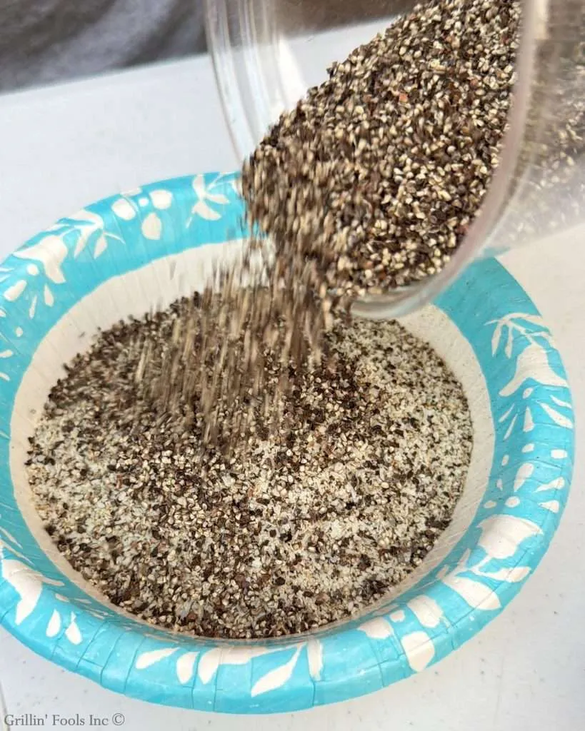 Very coarse pepper pouring into a paper bowl filled with SPG seasoning