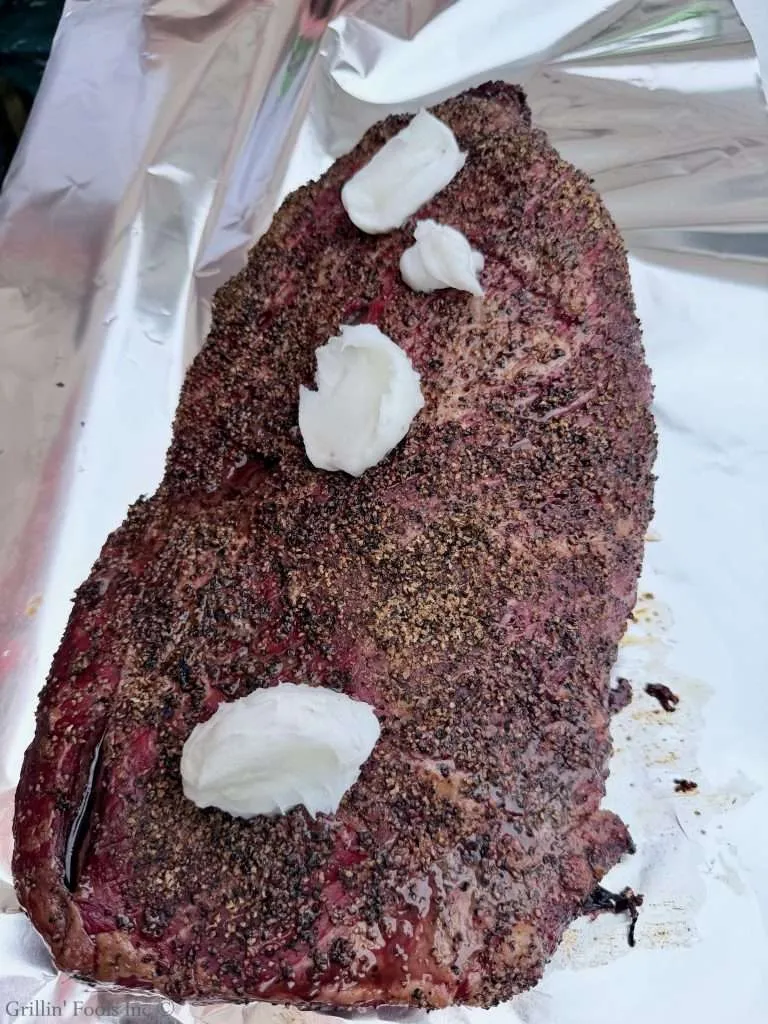 Smoked beef brisket with a pepper crust on foil, topped with dollops of beef tallow