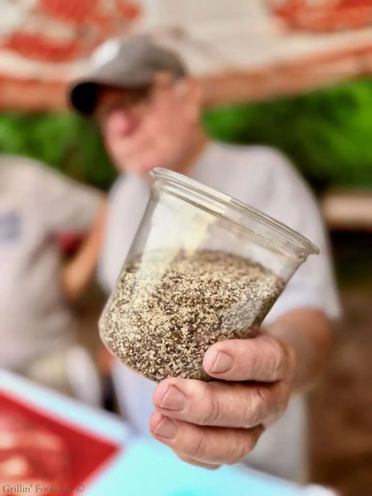 A man holding a jar of SPG seasoning with extra pepper that will be used for a dry brine on a brisket