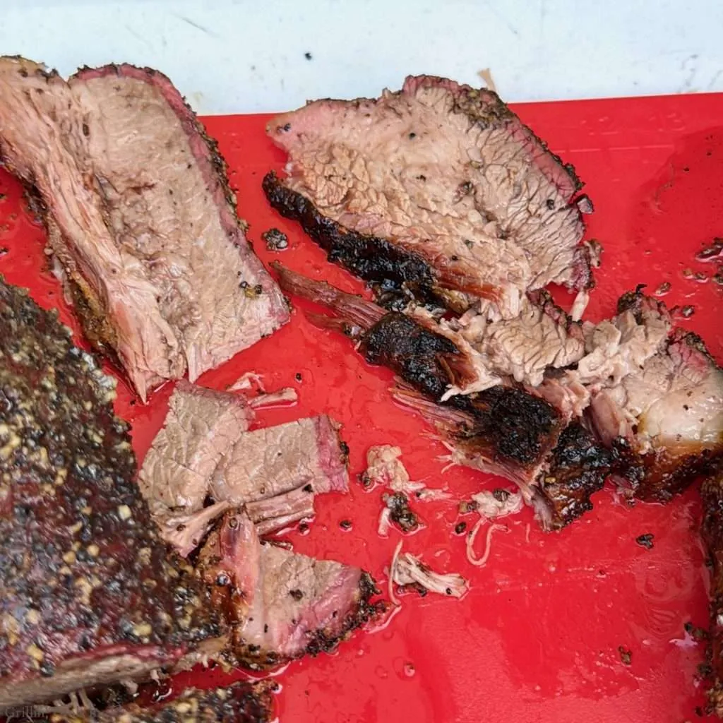 Slices of smoked beef brisket with charred crust on a red cutting board.