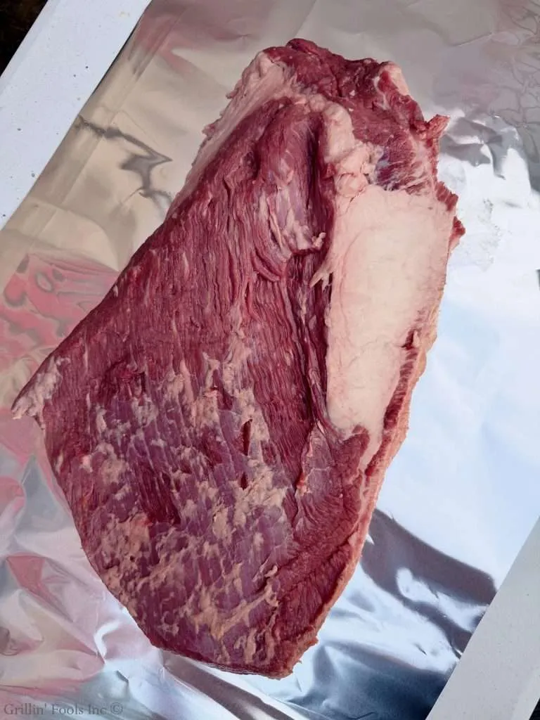 A raw packer brisket after trimming, fat cap down on a sheet of aluminum foil
