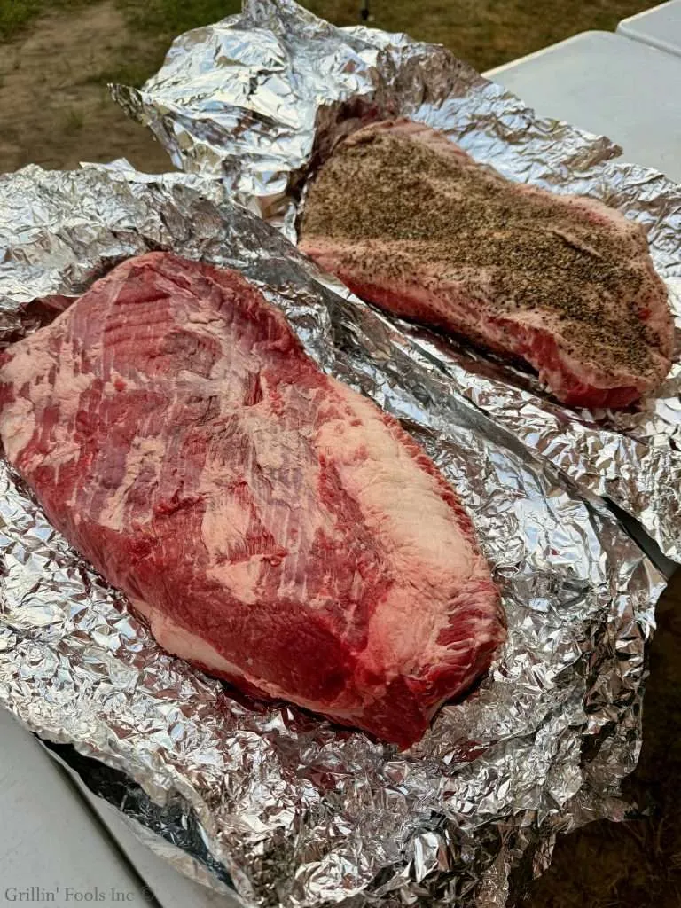 Two beef briskets, one slathered in seasoning and the other bare, both on aluminum foil