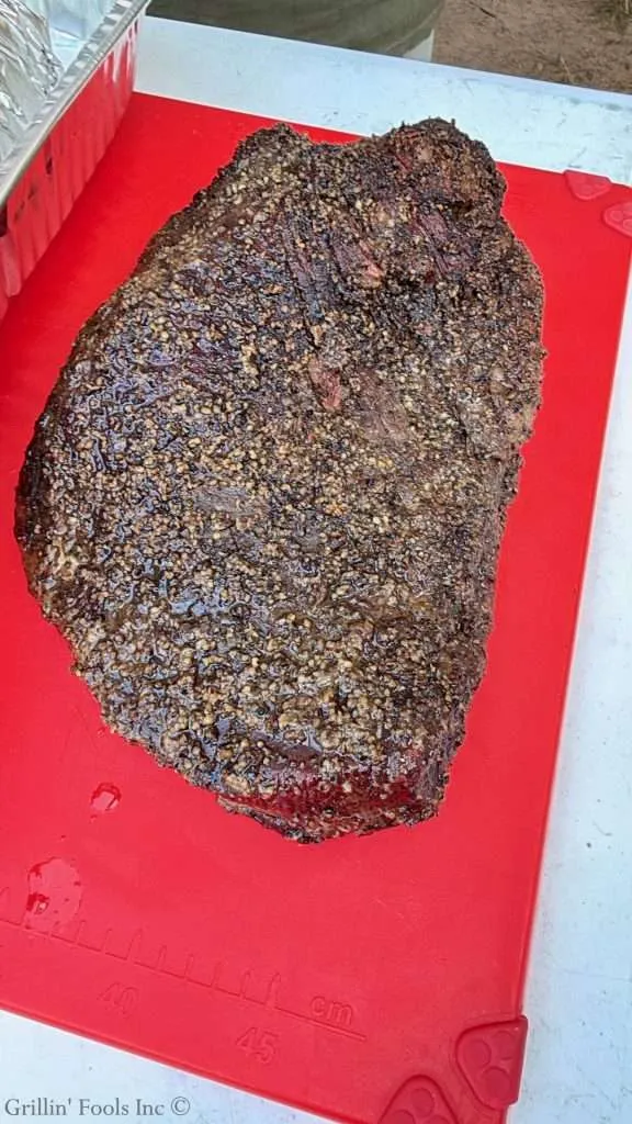 Large smoked beef brisket with a dark, textured bark on a red cutting board.