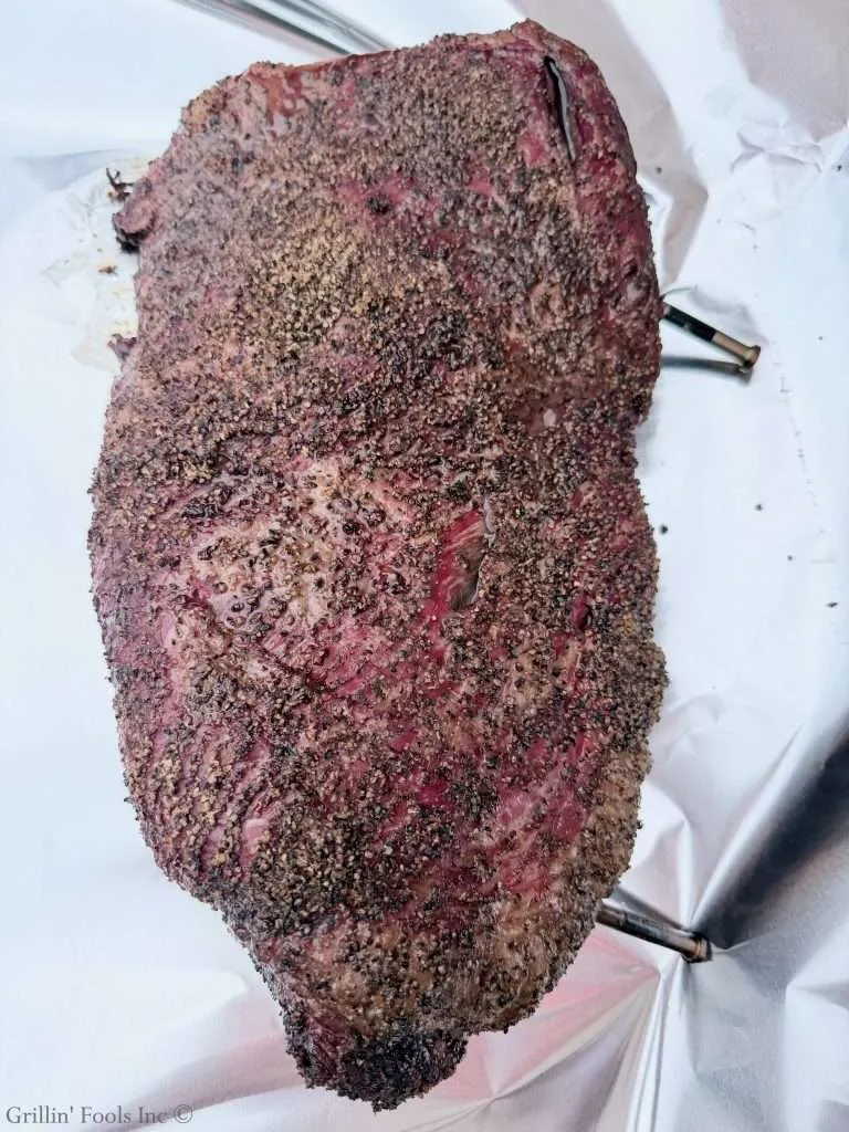 Smoked beef brisket with a dark pepper crust, resting on white parchment.