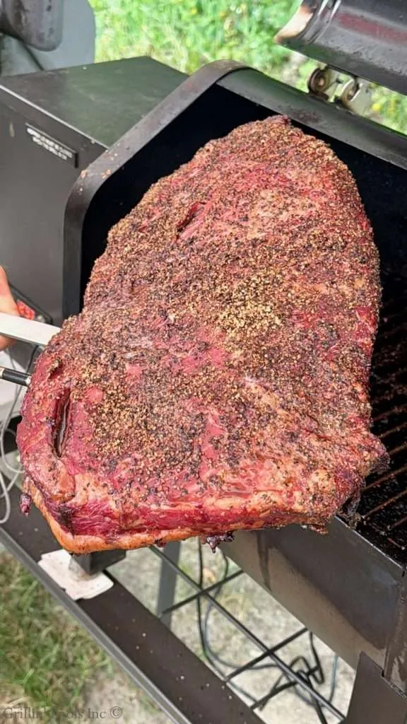 Large smoked beef brisket with a coarse pepper crust on a grill, ready for slicing