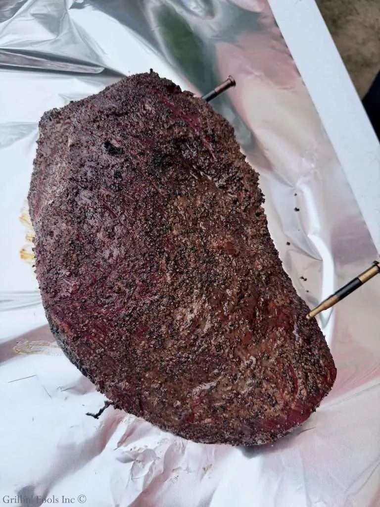 Bone-in smoked beef brisket with a dark bark resting on foil-covered surface.