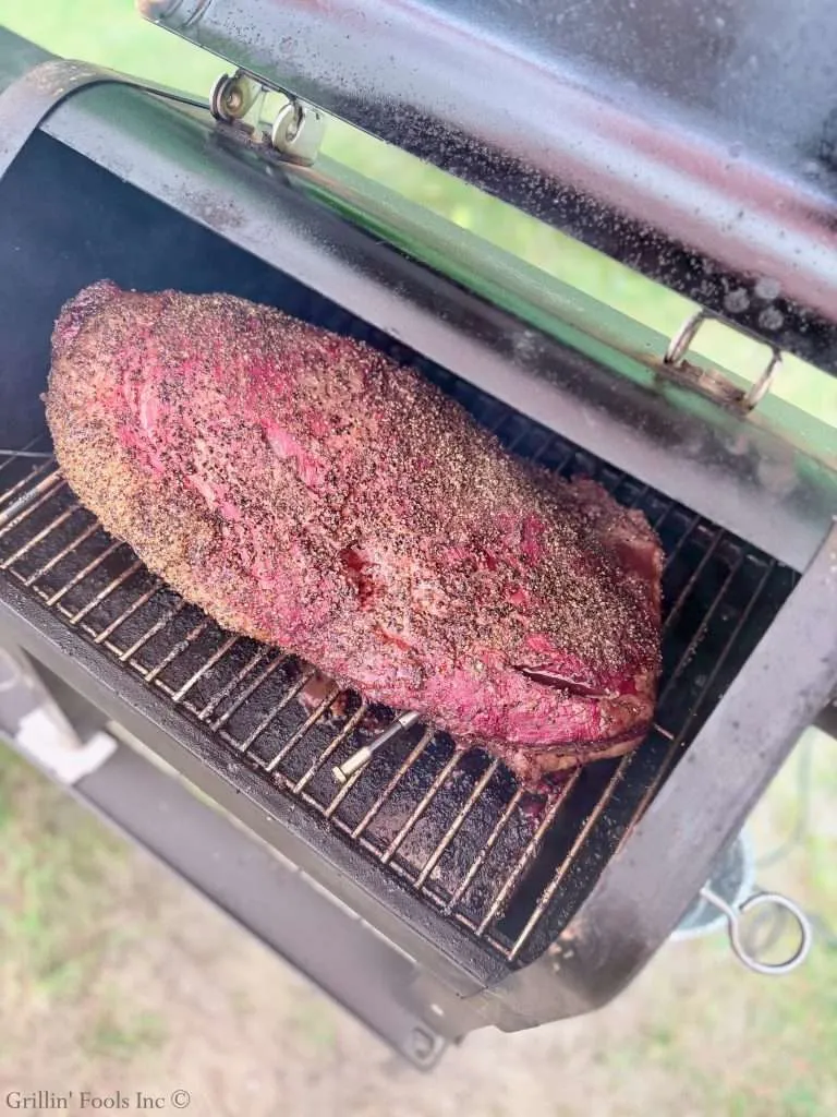 Beef brisket smoking on a barbecue grill with a dark bark and pink interior visible