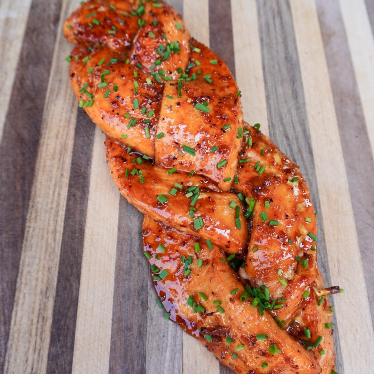 Smoked braided salmon on the cutting board topped with chives.