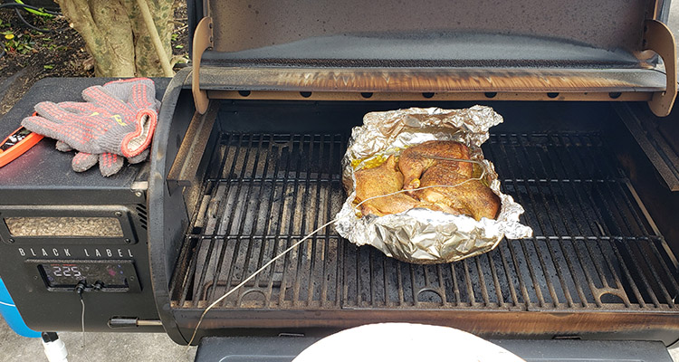 chicken wrapped in foil with a temperature probe on a pellet grill