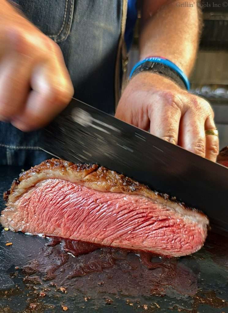 A man slices a picanha roast that is a beautiful rare and super juicy