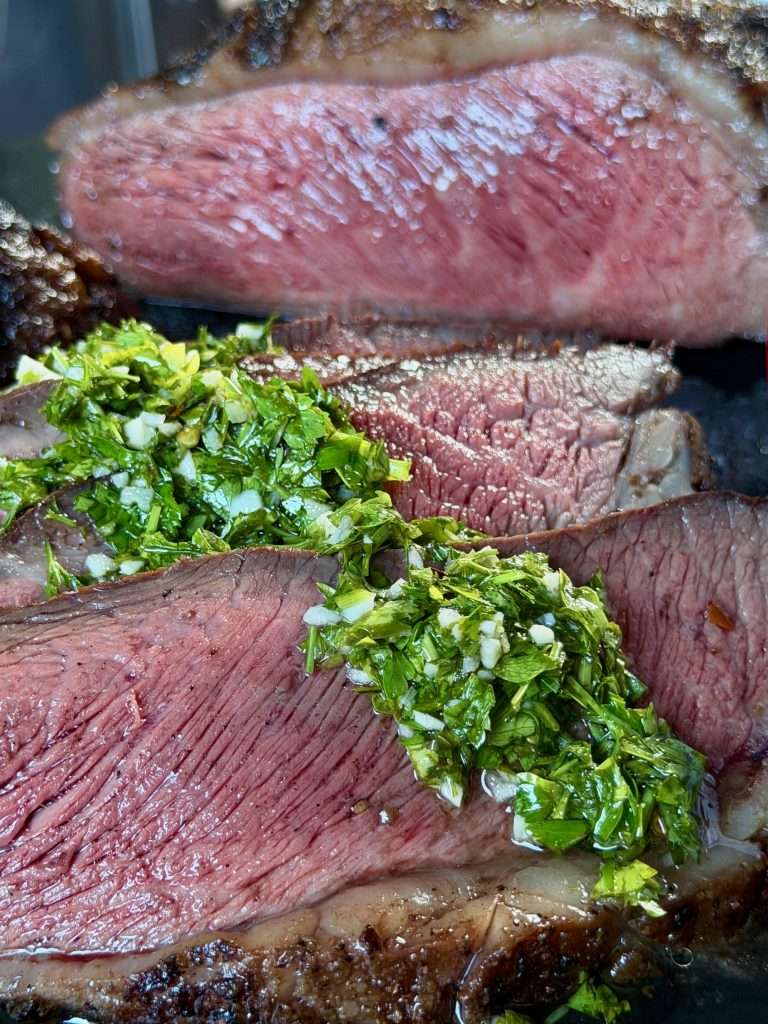 Fresh chimichurri spooned over medium rare sliced picanha steak