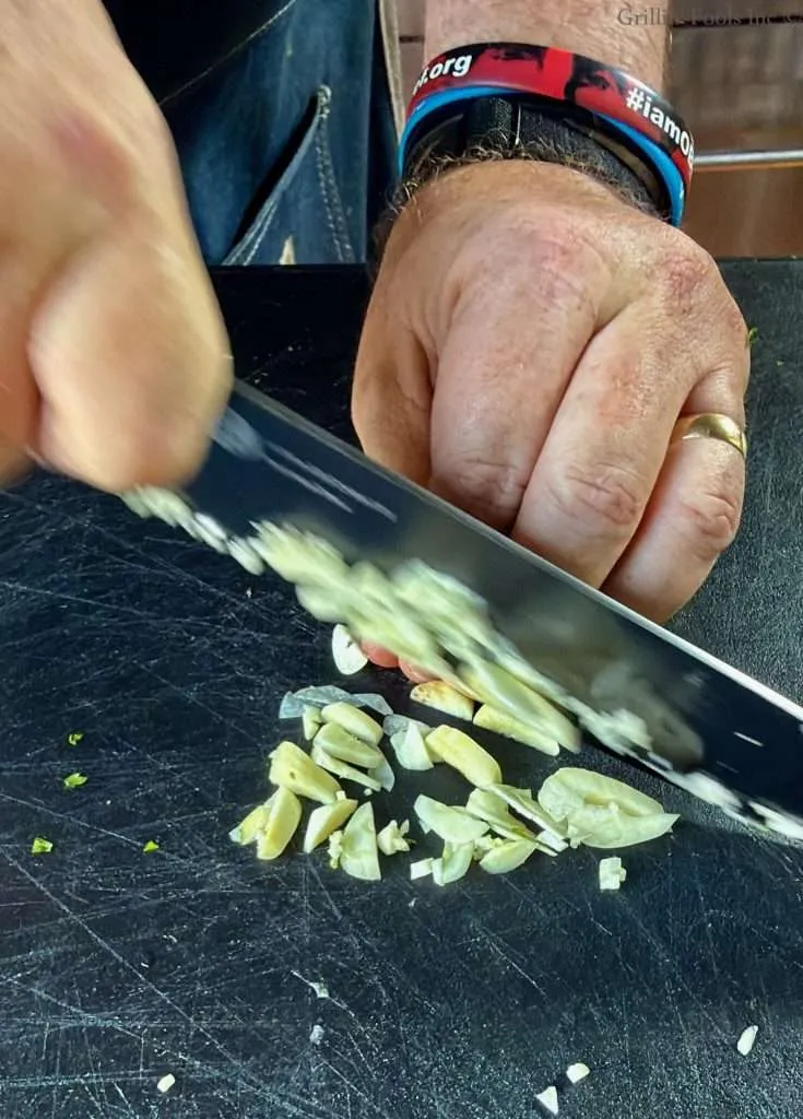 A man slices garlic with a black bladed knife on a black cutting board