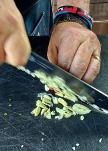 A man slices garlic with a black bladed knife on a black cutting board