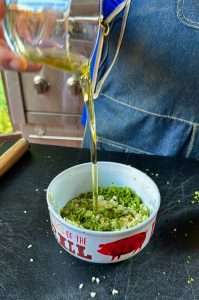 Pouring oil into a bowl of chimichurri sauce
