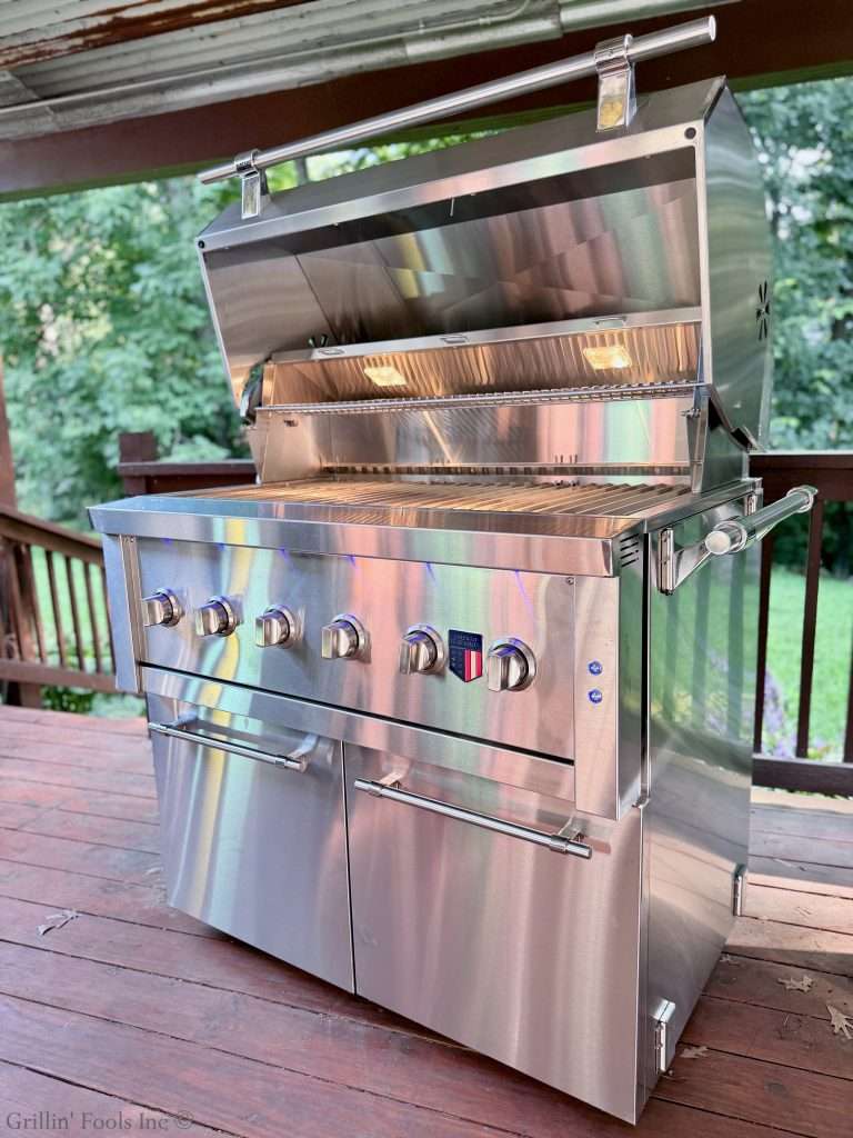 The American Made Grills, 42' Hybrid Ovation Grill on a deck with green foliage in the background