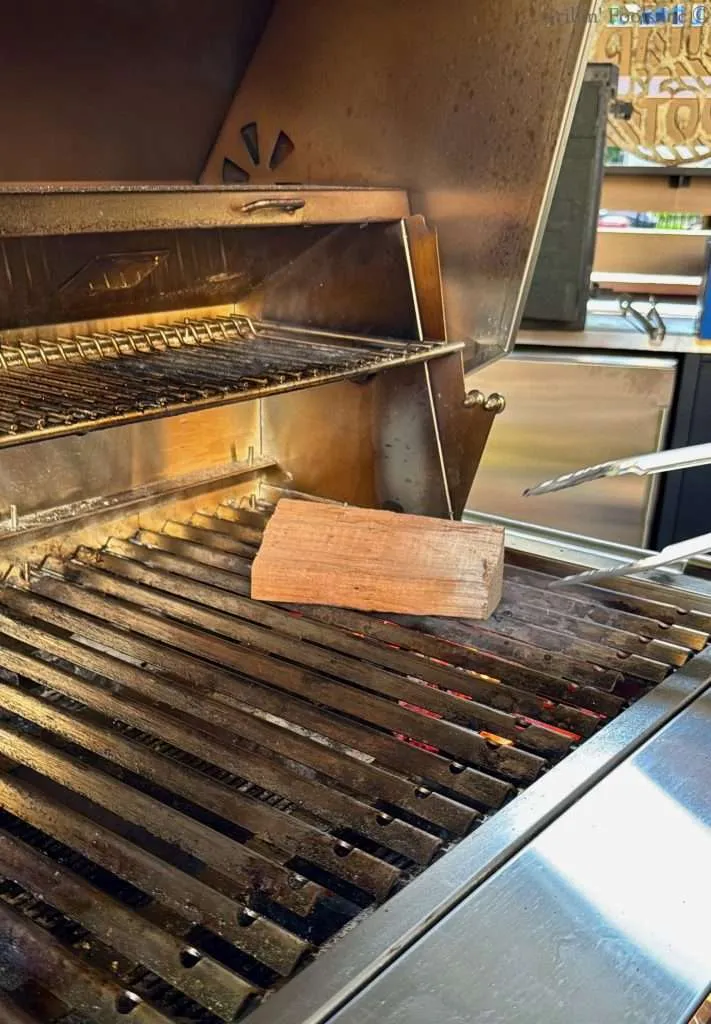 Two zone grilling set up on a charcoal grill with hot coals on the far side with a chunk of smoke wood on the grill grates above the hot coals.