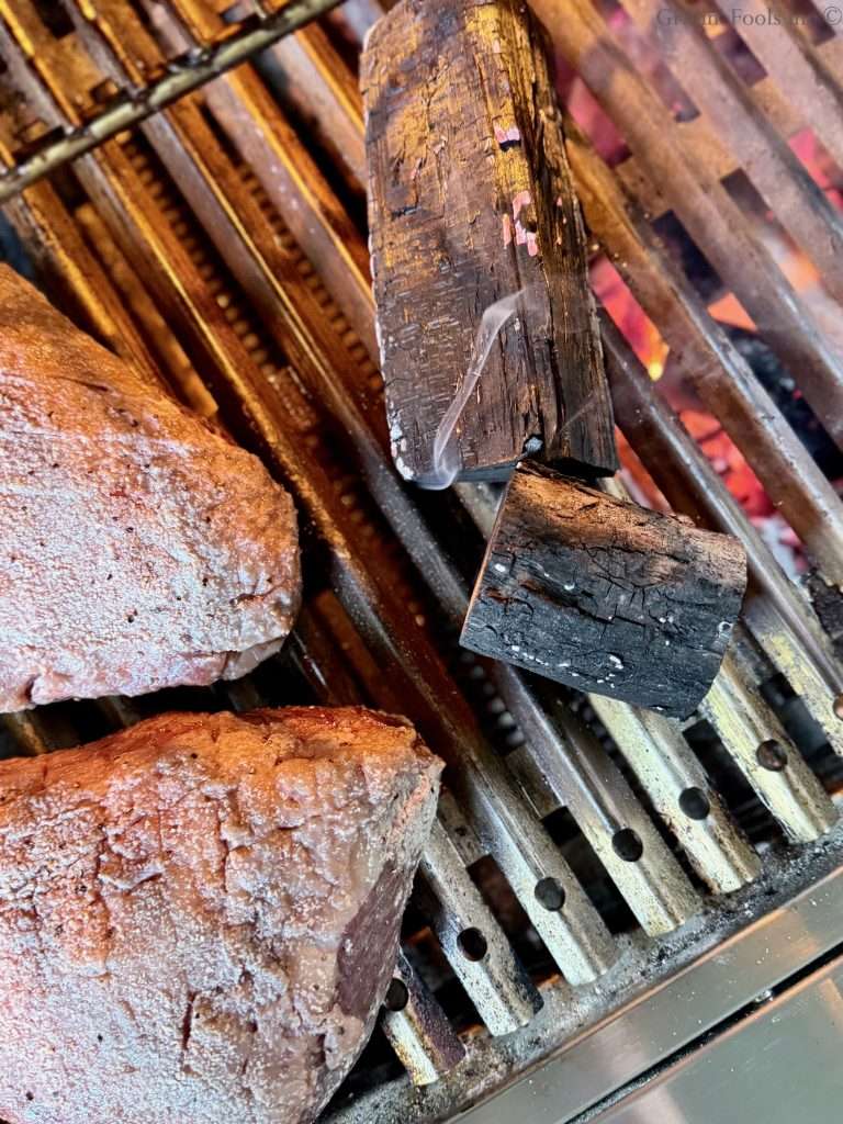 Charred wood smoking near two picanha roasts on a charcoal grill
