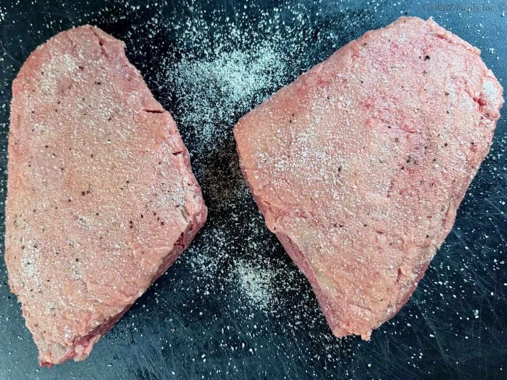 Two seasoned picanha roasts, fat cap up, on a black cutting board.