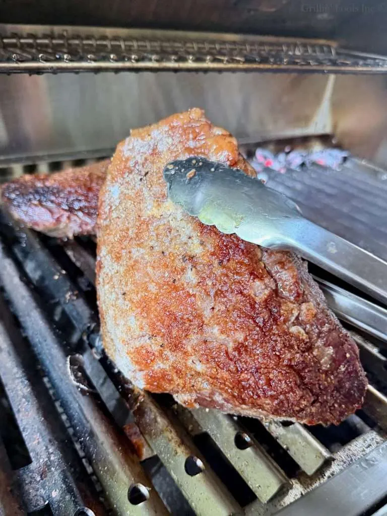 A roasted picanha roast being held by a pair of tongs.