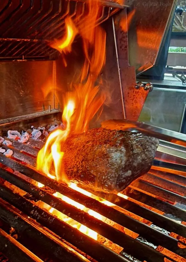 A picanha roast searing over a hot fire and flames kicking up from the fat rendering out of the fat cap.
