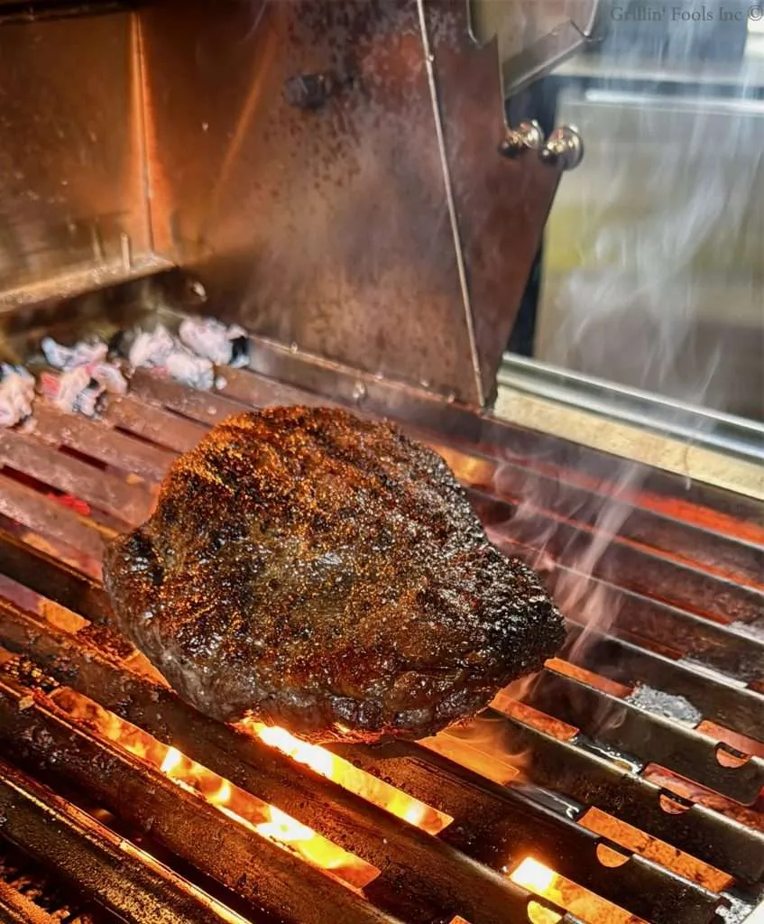 A picanha roast browning over hot coals on a charcoal grill