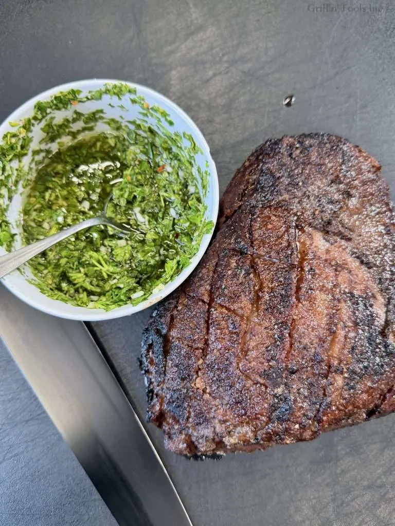 A roasted picaña next to a bowl of chimichurri