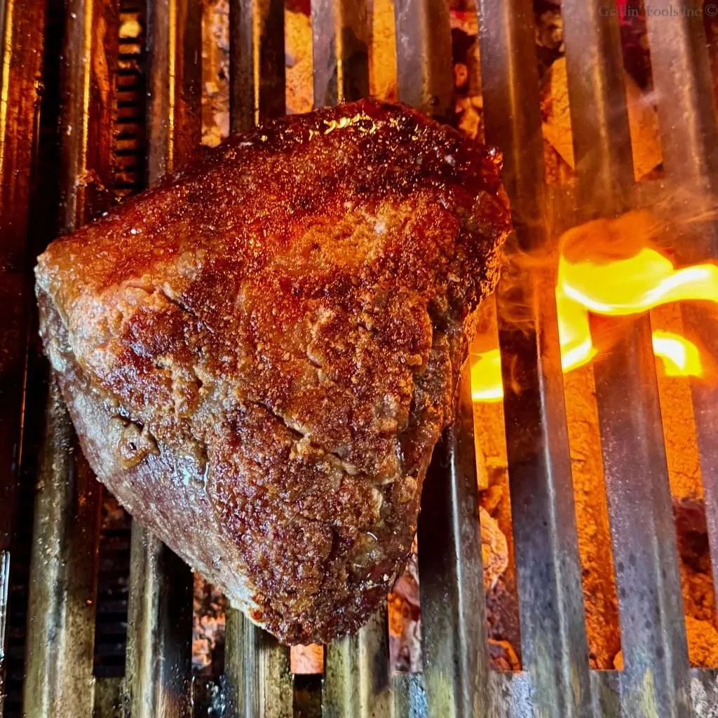 A picanha roast over hot coals on a charcoal grill