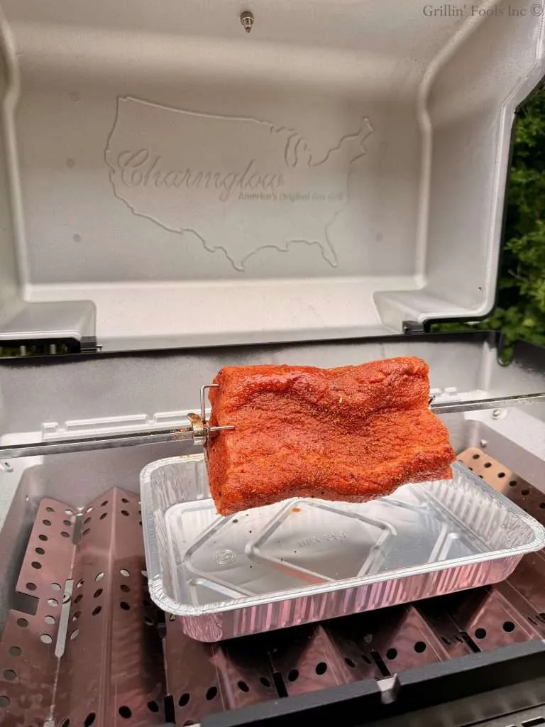 Seasoned pork loin on a rotisserie spit inside a Charmglow grill with an aluminum pan below