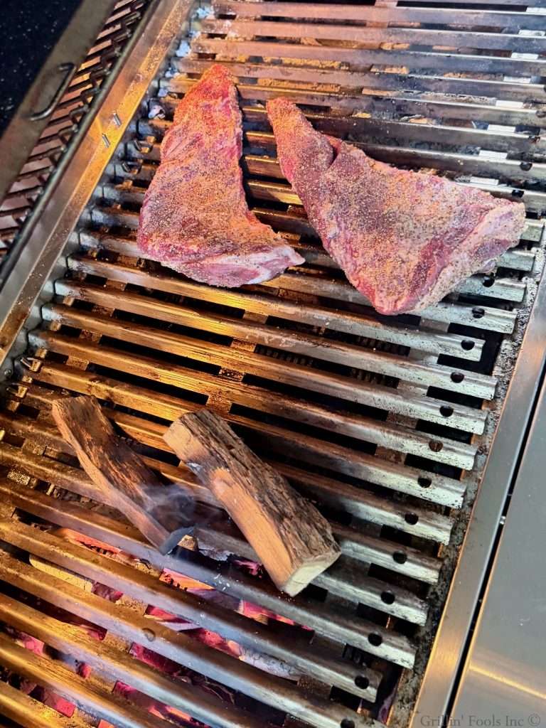 Two tri tips sitting a few inches off of the hot coals and smoldering smoke wood on a large grill