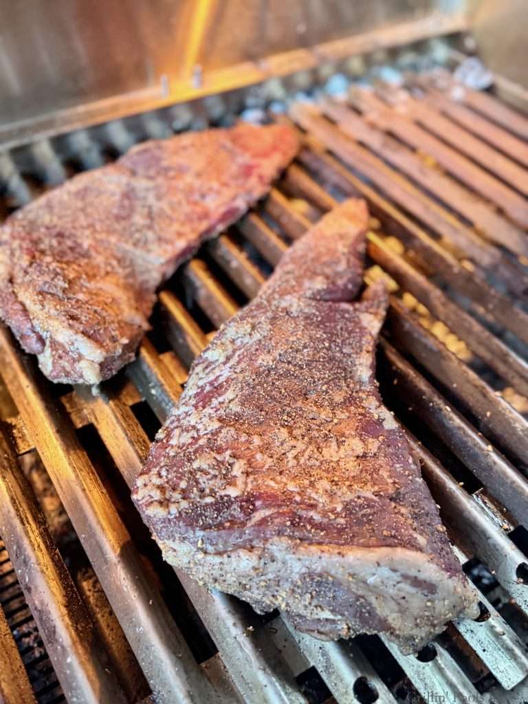 Two tri tips, partially cooked on a charcoal grill