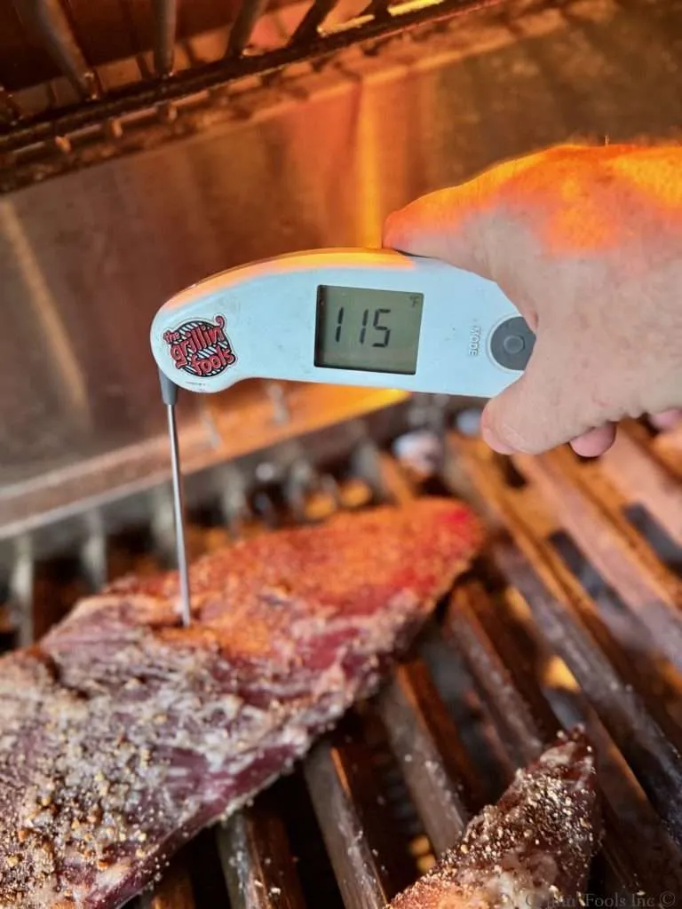 A tri tip roast reading 115F from a probe thermometer, all on a charcoal grill