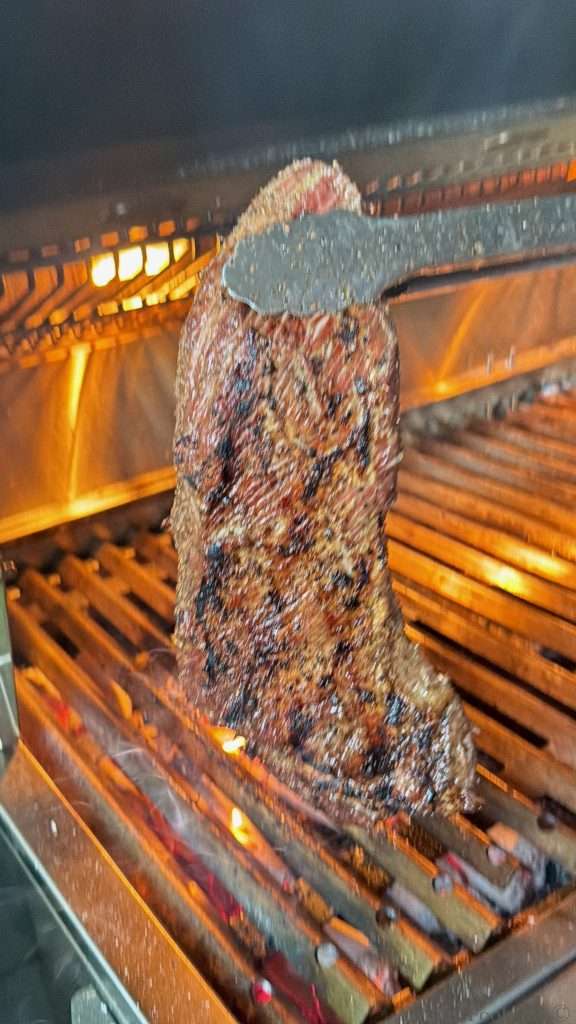Tongs holding a charred tri tip up over the hot coals on a charcoal grill