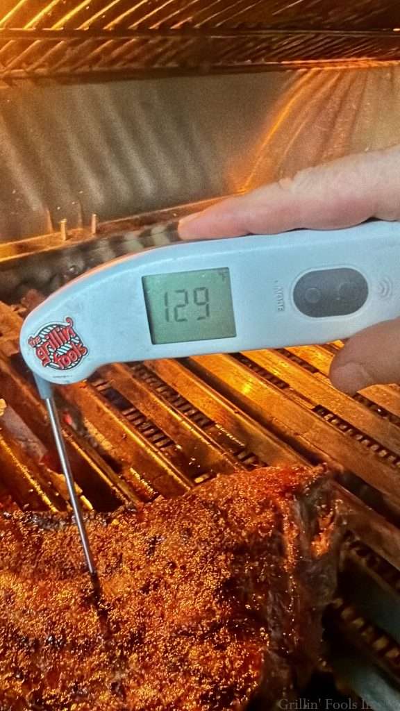A probe thermometer showing 129F while inserted into a tri tip on the grill