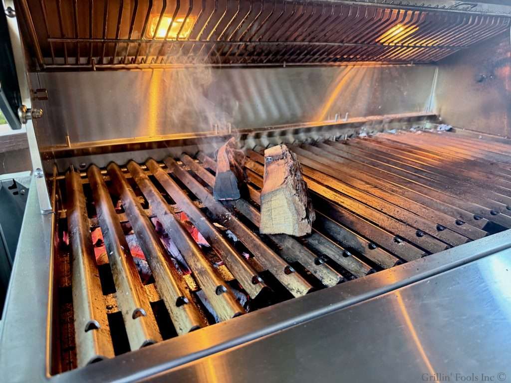 Smoke wood smoldering on the grill off to the edge of the hot coals