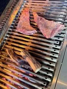 Two tri tips sitting a few inches off of the hot coals and smoldering smoke wood on a large grill