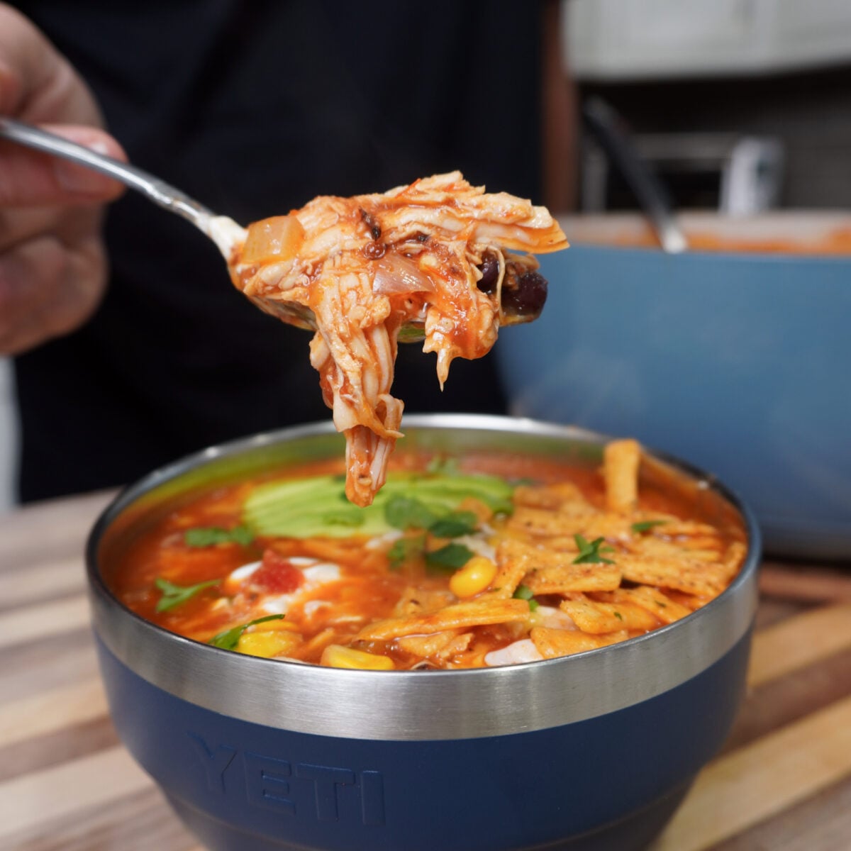 Chicken tortilla soup on a spoon over a plated bowl.