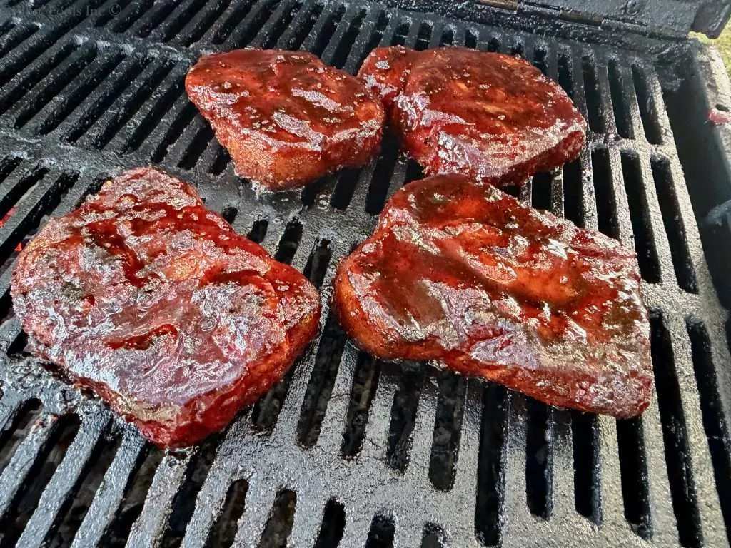 Four sauced pork collars on a charcoal grill