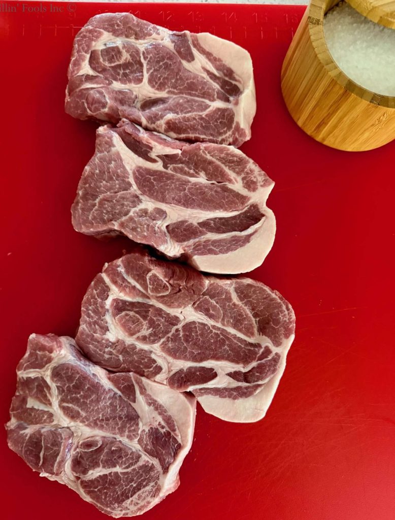 Four pork collars on a red cutting board next to a container of salt