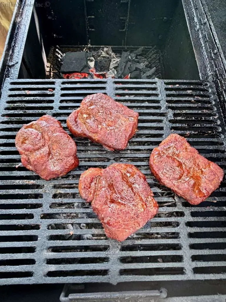 Four seasoned pork collars on the cool, near side of the grill while coals burn on the far side of the grill
