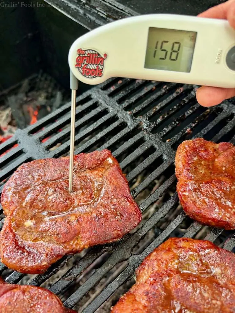 A probe thermometer reading 158F on a charcoal grill