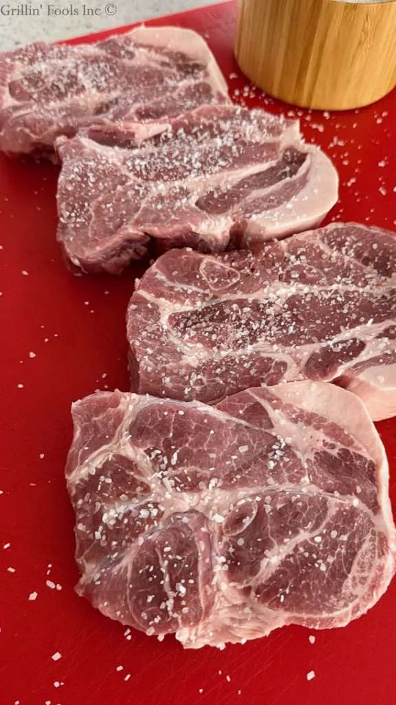 Pork collar seasoned with coars salt on a red cutting board